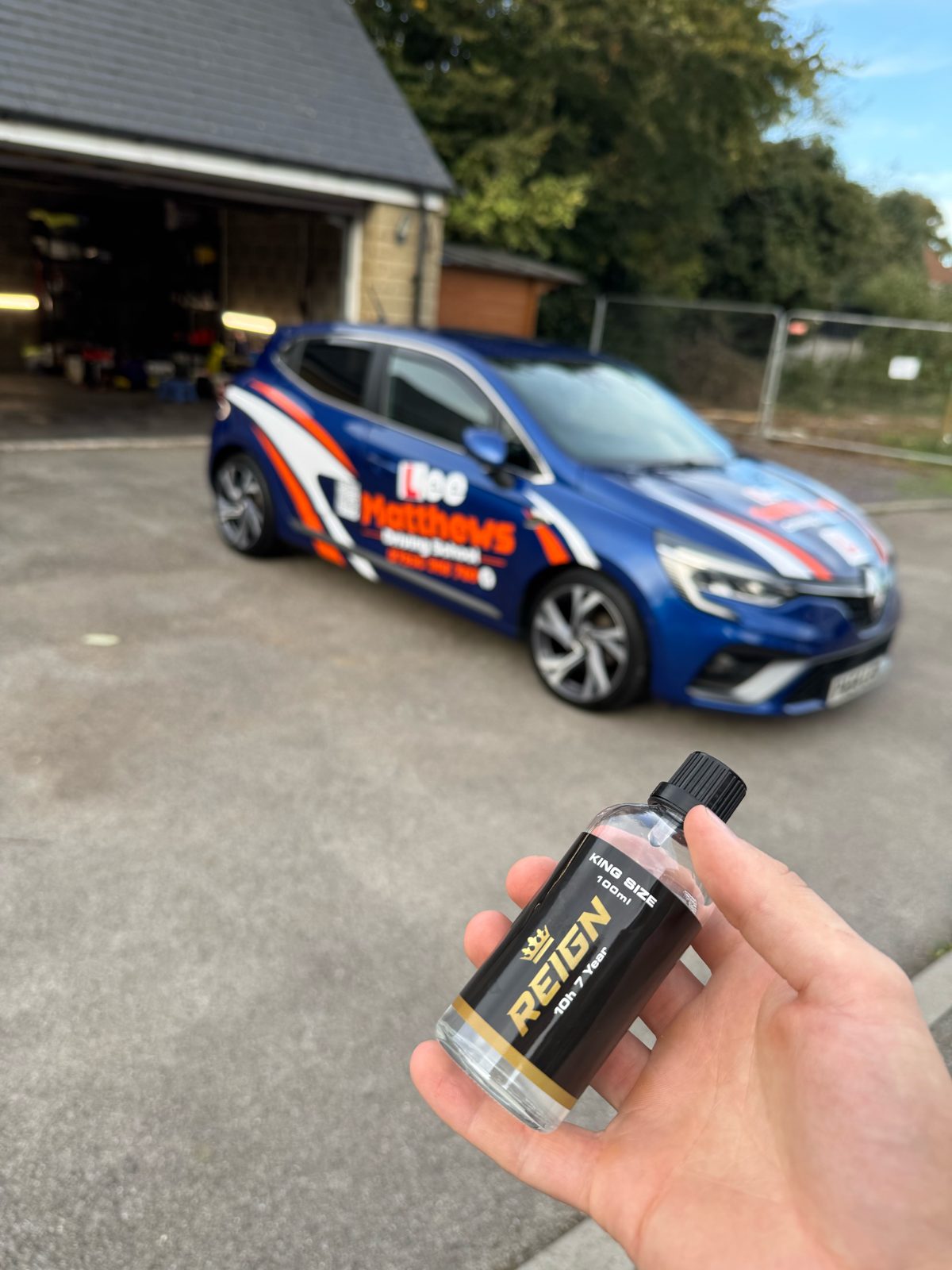 Renault Clio driving-school car at the Washy Luxe Glapwell unit, with a bottle of REIGN 7-year ceramic coating held up in front
